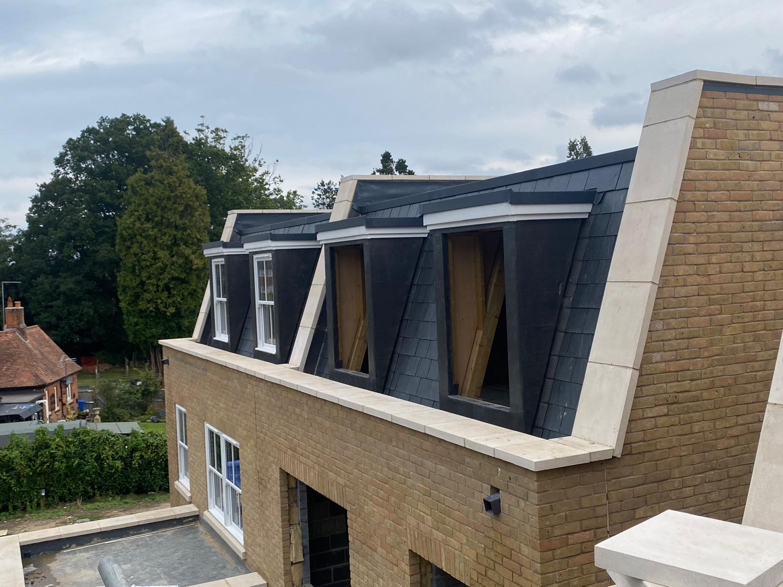 DM Roofing — completed natural slate mansard roof with dormers and stone coping, high-end residential new build